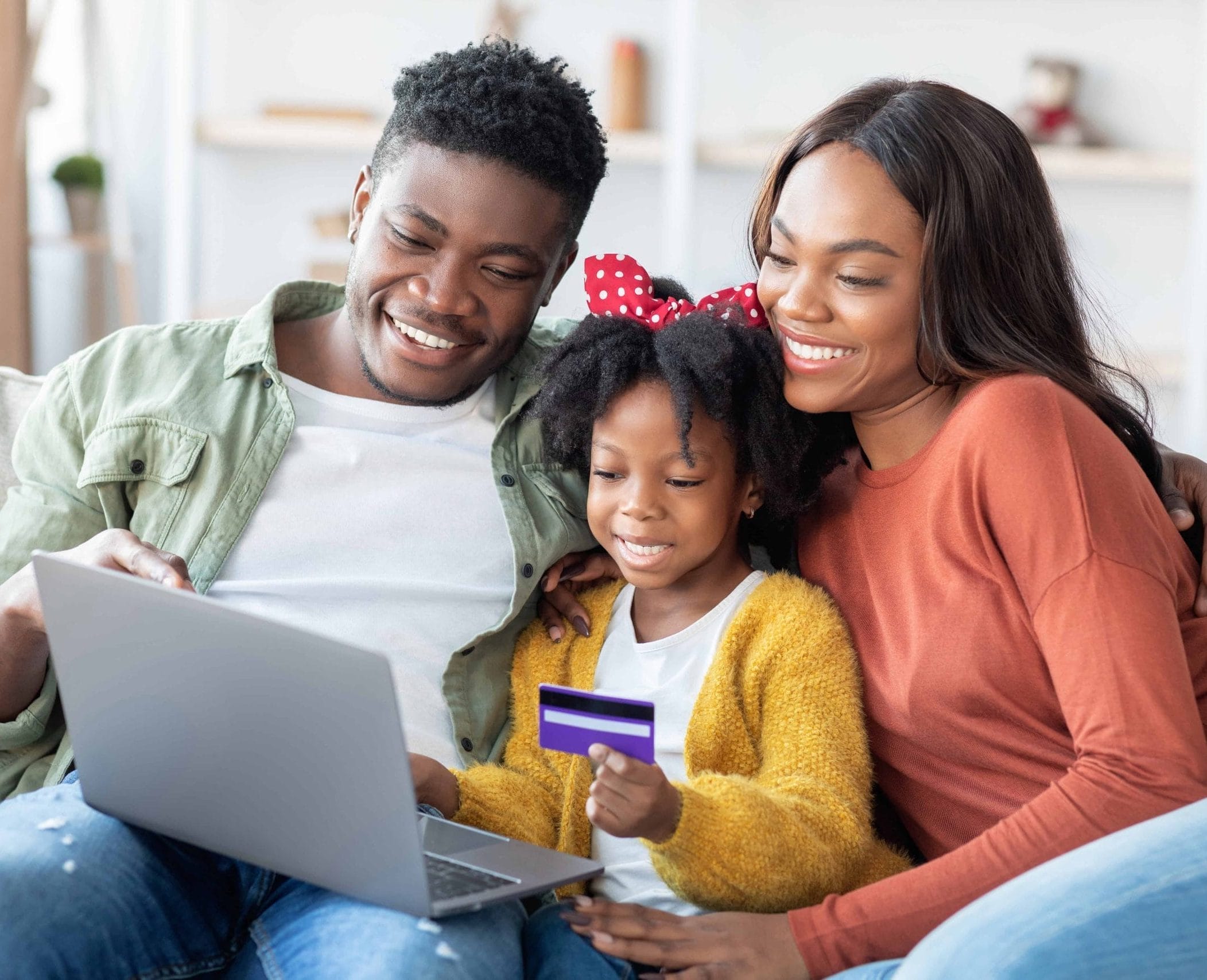 Black family on the couch teaching their young daughter about credit